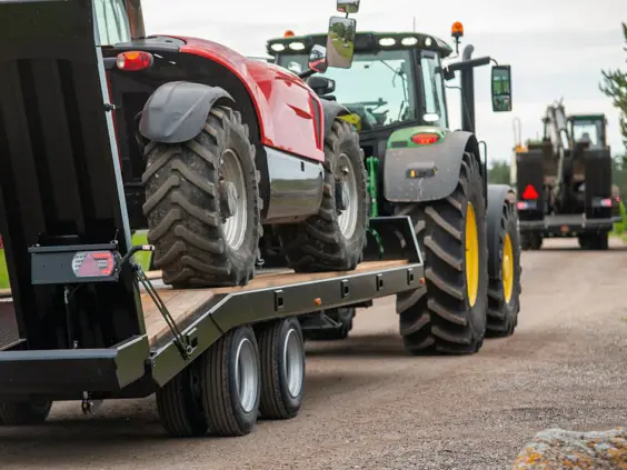 En robust Palmse PT5750 maskintralle som frakter en rød traktor på en grusvei.