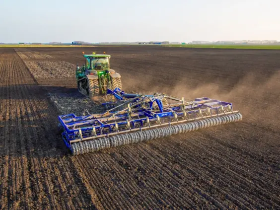 En grønn traktor trekker en blå DALBO Rollomaximum såbedsharv over et stort jorde.