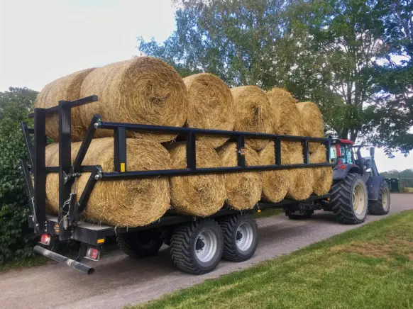 Palmse PT3750PS plattformhenger fullastet med runde halmballer bak en traktor på en vei.