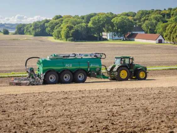 En John Deere traktor som trekker en grønn SAMSON PG II Genesis på en åker.