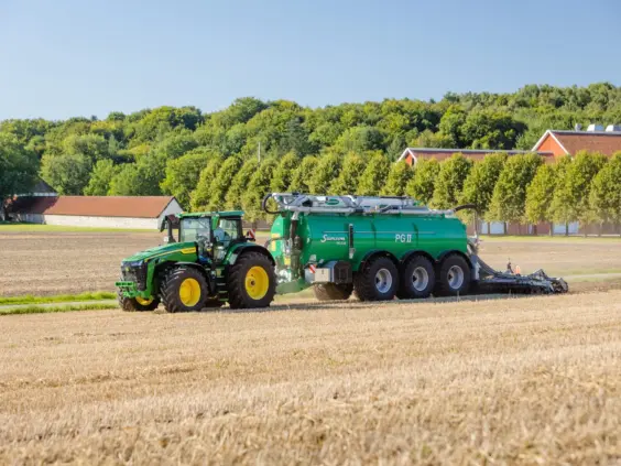 En grønn traktor trekker en SAMSON PG II Genesis gjødselvogn over en åker.