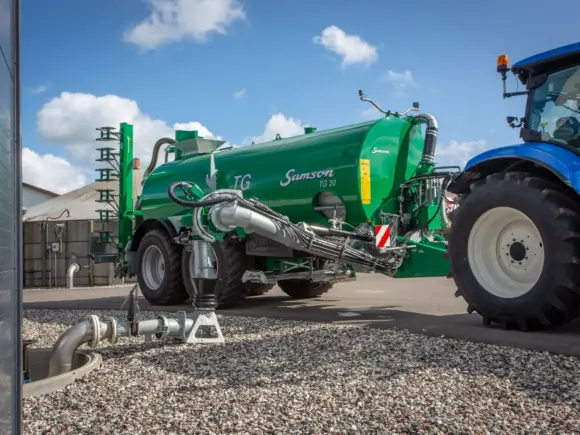 Samson TG 20 gjødselvogn koblet til en blå traktor på en gårdsplass.