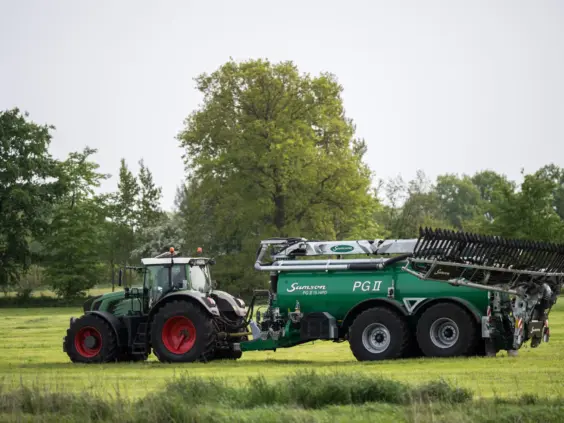 En grønn traktor trekker en SAMSON PG II Genesis gjødselvogn over en gresskledd mark.