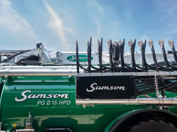 Grønn SAMSON PG II Genesis gjødselvogn med avansert sprederutstyr mot en blå himmel.