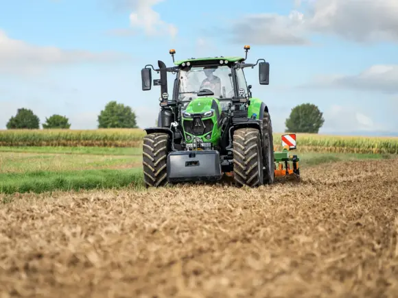 En grønn Deutz-Fahr Series 6.4 traktor som arbeider på en åker under blå himmel.