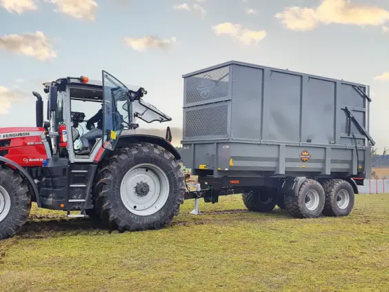 En rød traktor som trekker en Palmse PT1900MB dumperhenger på en gressplen.