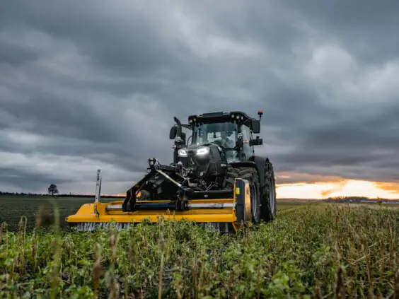 En sort Deutz-Fahr Series 6C traktor med gult utstyr på en åker ved solnedgang.