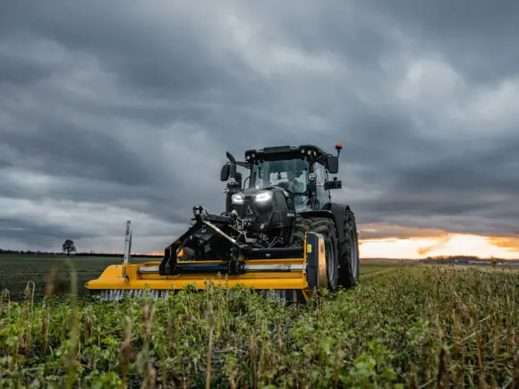 En sort Deutz-Fahr Series 6C traktor med gult utstyr på en åker ved solnedgang.