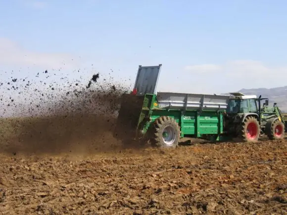 En Samson SP-serien tørrgjødselvogn sprer gjødsel på en åker bak en traktor.