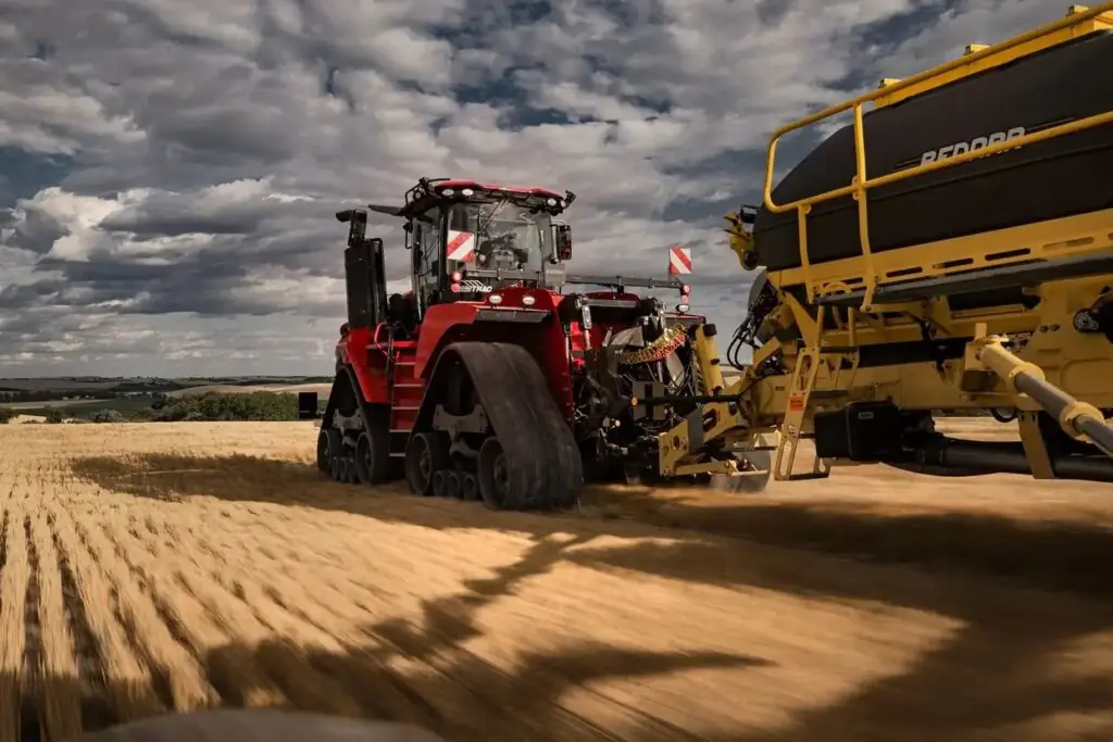 Kraftig rød Steiger 785 Quadtrac traktor med belter som trekker landbruksutstyr over en gyllen åker.