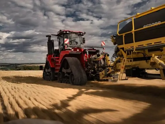 Kraftig rød Steiger 785 Quadtrac traktor med belter som trekker landbruksutstyr over en gyllen åker.