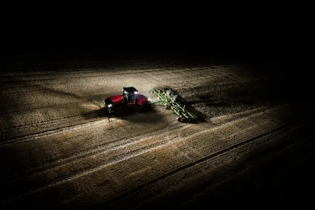 En rød Steiger 785 Quadtrac traktor arbeider på en åker om natten med kraftig belysning.