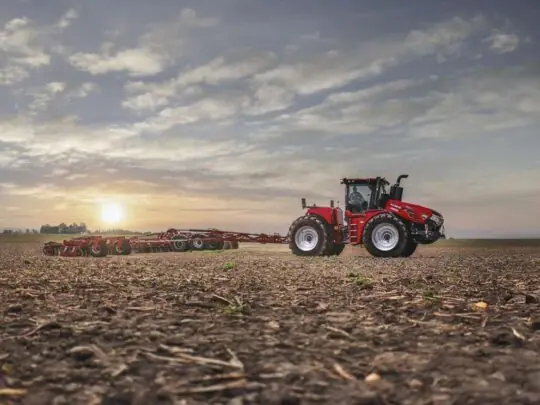 En rød Steiger 785 Quadtrac traktor i arbeid på en åker under en vakker solnedgang.