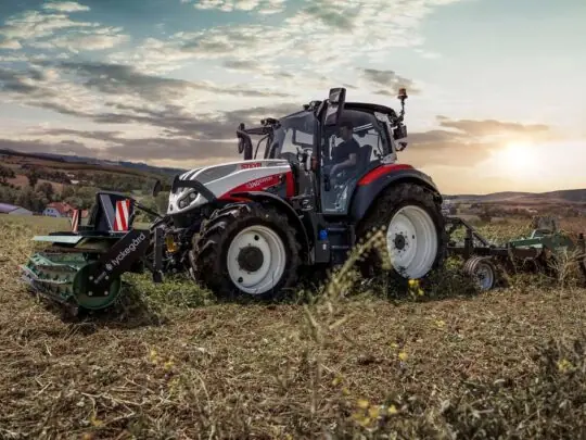 Rød Steyr Expert S-Control 8 traktor i arbeid på en åker ved solnedgang.