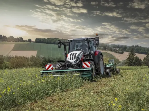 Steyr Expert traktor i arbeid på en åker under en dramatisk himmel ved solnedgang.