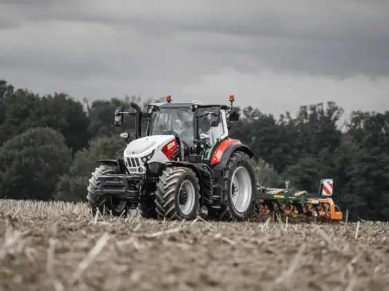 Steyr Impuls traktor i arbeid på en åker med landbruksutstyr bak.
