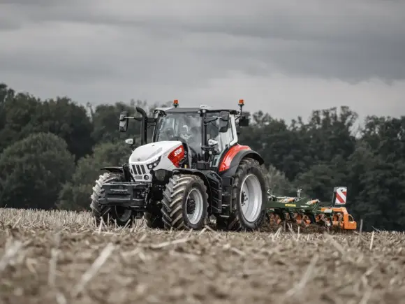 Steyr Impuls traktor i arbeid på en åker med landbruksutstyr bak.