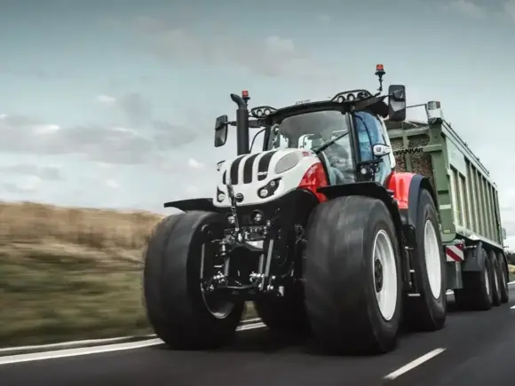 Rød og hvit Steyr Terrus CVT traktor i fart på vei med grønn tilhenger.