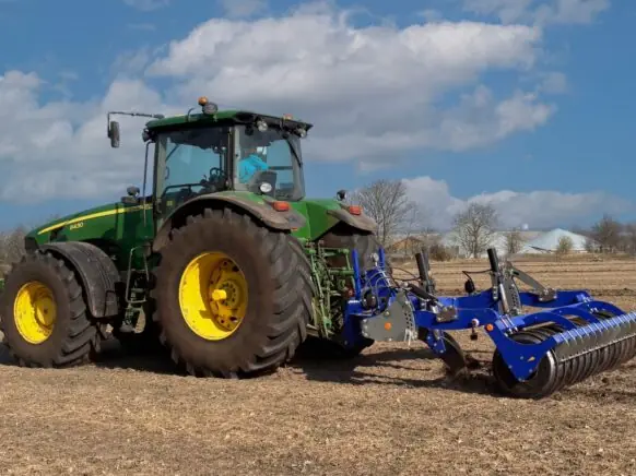 Grønn John Deere traktor på en åker med en blå DALBO Subsoiler montert bak.