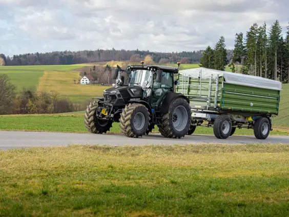 Svart Deutz-Fahr Series 6C traktor med grønn tilhenger på vei i et vakkert landskap.