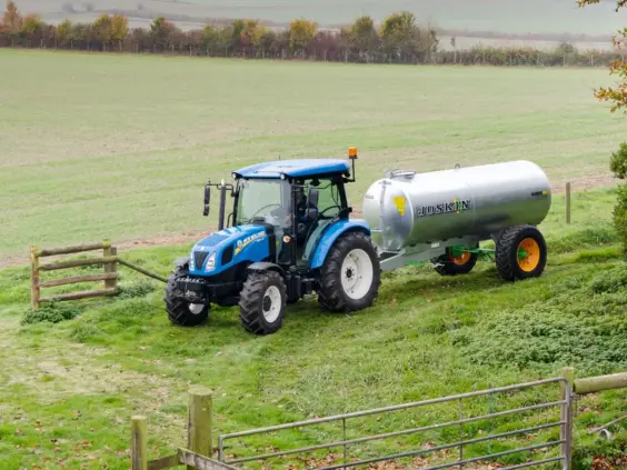 Blå New Holland T4S traktor med en Joskin-tankvogn på et grønt jorde.