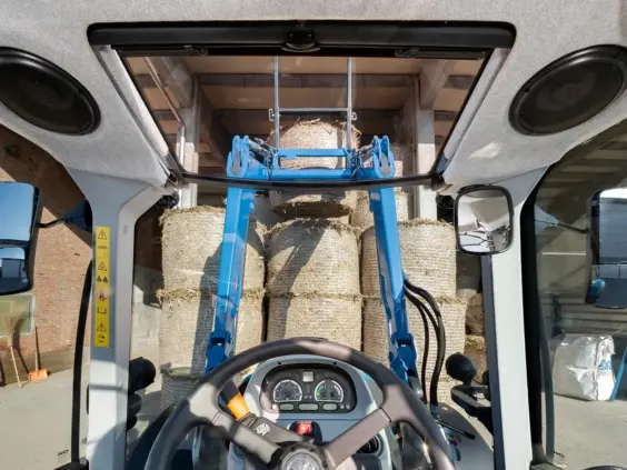 Førerhusutsikt fra T5 Dynamic Command og Auto Command som løfter halmballer med en blå frontlaster.