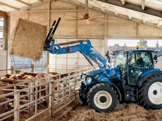 Blå T5 Dynamic Command og Auto Command traktor som løfter en halmball i et fjøs.