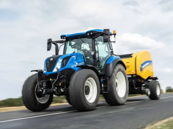 Blå New Holland T5 Dynamic Command og Auto Command traktor på vei med utstyr.