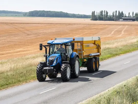 Blå traktor T5 Dynamic Command og Auto Command med gul Joskin-tilhenger på vei.