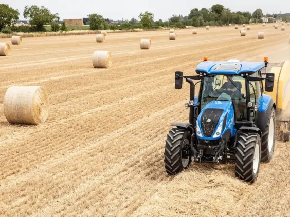 En blå traktor, T5 Dynamic Command og Auto Command, lager høyballer på en åker.