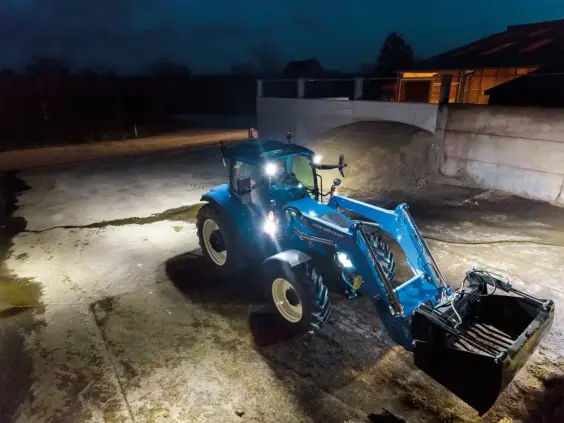 Blå New Holland T5 Electro Command traktor med frontlaster som arbeider ute om natten.