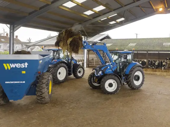 Blå New Holland T5 Electro Command traktor som laster materiale i en West-tilhenger.