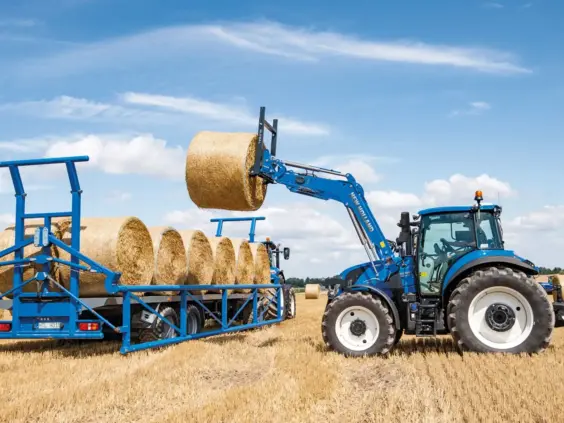 Blå New Holland T5 Electro Command traktor som løfter en rundballe på en åker.