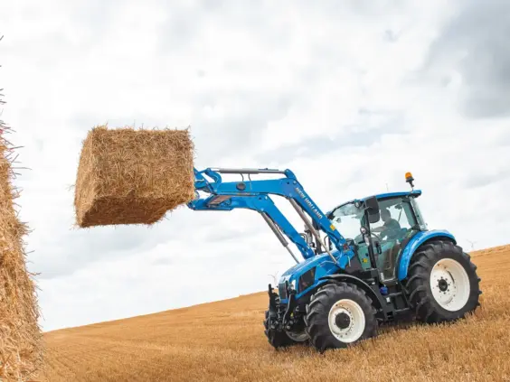 Blå New Holland T5 Utility traktor løfter en stor halmball på en åker.