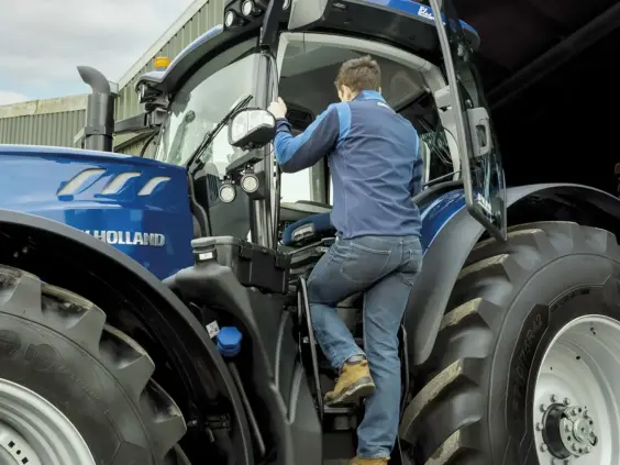 En person klatrer inn i førerhuset på en blå New Holland T7 Heavy Duty traktor.