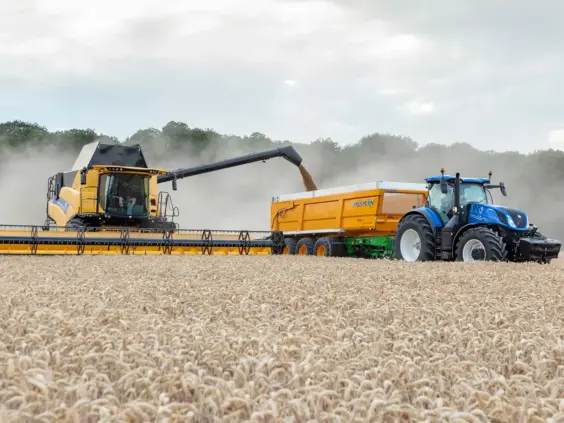 En blå New Holland T7 Heavy Duty traktor ved siden av en skurtresker i arbeid.