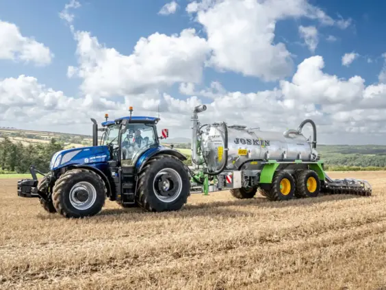 New Holland T7 LWB med PLM Intelligence trekker en Joskin-vogn over en høstet åker.