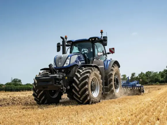 Blå New Holland T7.270 Methane Power traktor som arbeider på en gyllen kornåker.