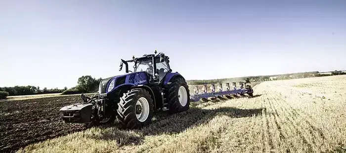 En mørkeblå New Holland T8 Genesis traktor pløyer en åker på landsbygda.