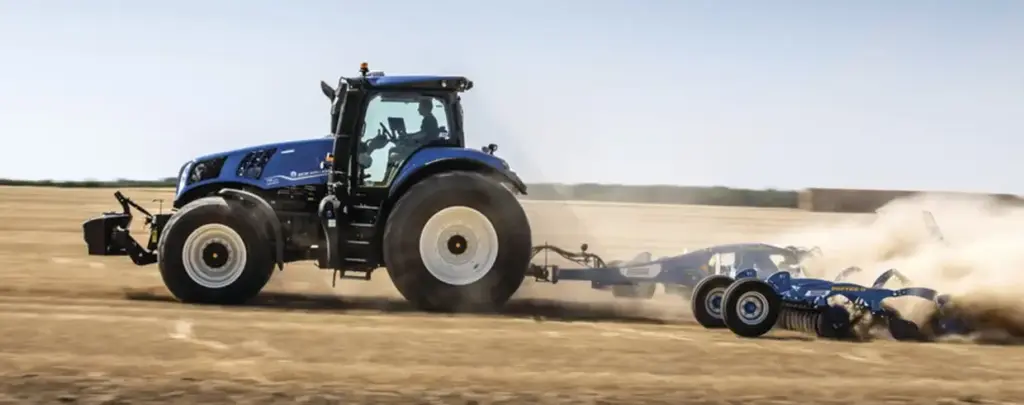 En blå New Holland T8 Genesis traktor som arbeider på en tørr åker.