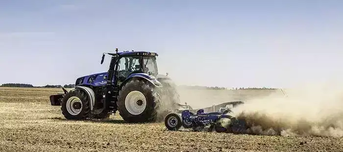 En blå New Holland T8 Genesis traktor som arbeider på en tørr åker.