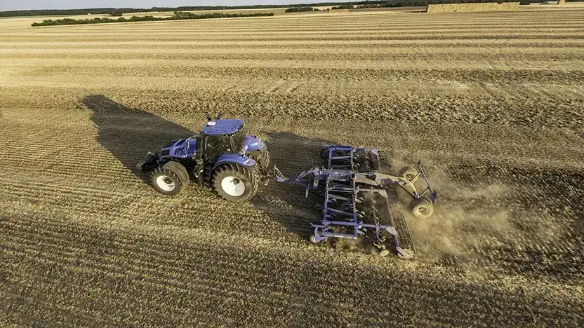 En blå New Holland T8 Genesis traktor trekker harv på en stor åker.