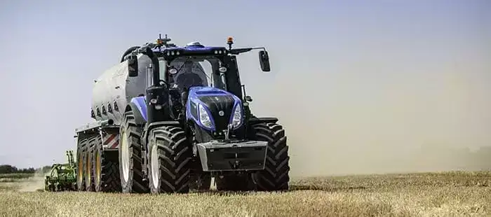 En blå New Holland T8 Genesis traktor i arbeid på en tørr åker.