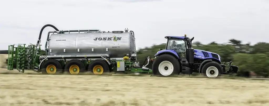 Blå New Holland T8 Genesis traktor som trekker en stor Joskin-tank på en åker.