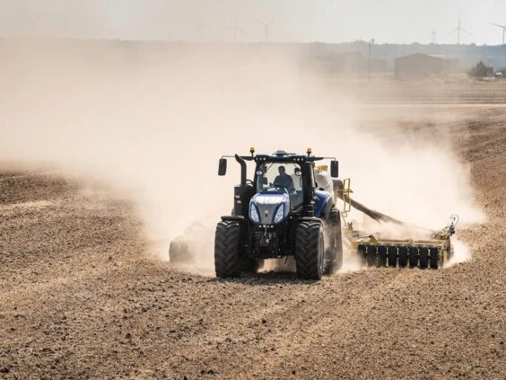 En blå New Holland T8 Genesis traktor i arbeid på en støvete åker.