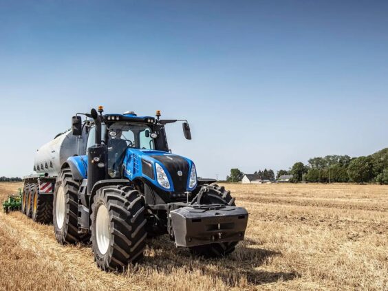 Blå New Holland T8 Genesis traktor med tankvogn på en høstet åker.