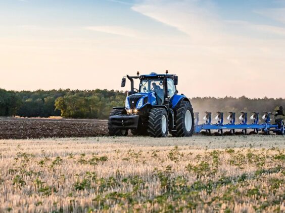 En blå New Holland T8 Genesis traktor pløyer en åker under en klar himmel.