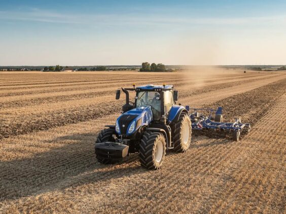 En blå New Holland T8 Genesis traktor som arbeider på et jorde om høsten.