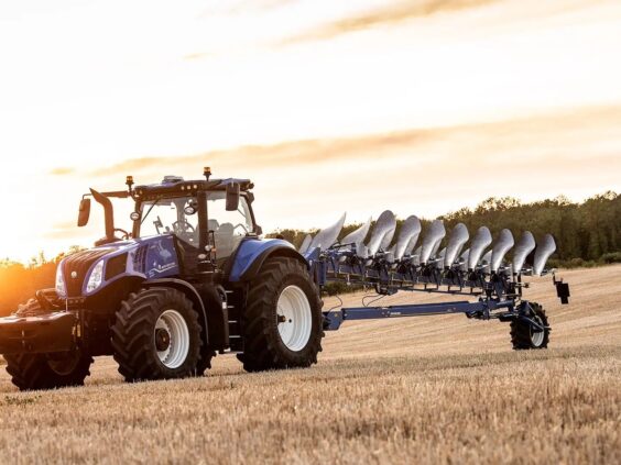 En blå New Holland T8 Genesis traktor med plog på en åker under solnedgang.
