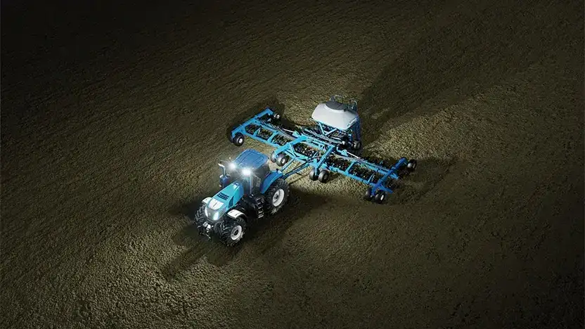 En blå New Holland T8 Genesis traktor som arbeider på en åker om natten.